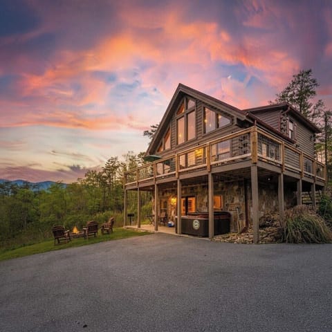 The lodge at dusk — wraparound deck, hot tub, and fire pit, mountains behind.