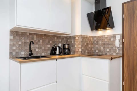 A minimalist kitchen with white cabinetry, light wood countertops, and a textured backsplash. Small appliances, including a kettle and coffee machine, are neatly arranged for convenience.