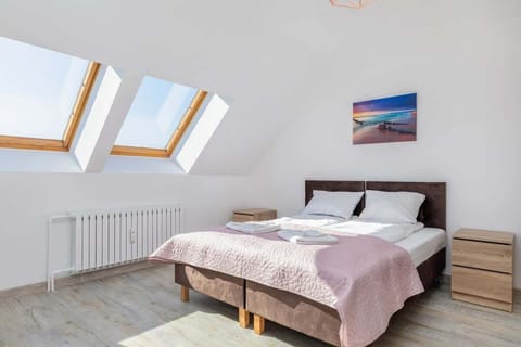 A cozy bedroom with a comfortable double bed covered in a pink bedspread, a landscape painting hanging above it, and a wooden bedside table next to the bed.