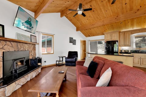 Cozy mountain living room with a stone fireplace, comfy seating, and smart TV—perfect for relaxing evenings, movie nights, and warm cabin vibes after outdoor adventures.