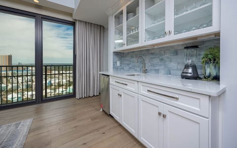This sleek wet bar features white cabinetry, a stylish backsplash, a blender, and a stunning view through large glass doors