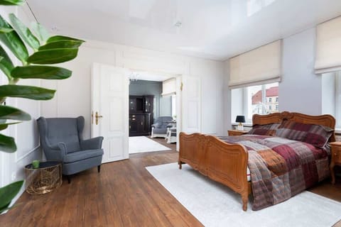 A cozy bedroom with a double bed and wooden furniture. Large windows allow natural light to brighten the space.