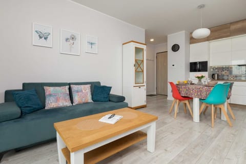 A modern living room with a teal sofa, a wooden coffee table, and wall decorations. The room has a bright and cozy atmosphere with stylish furniture.