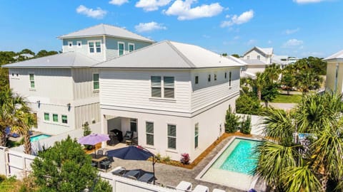 Take in an aerial perspective of this coastal retreat, highlighting the private back patio, custom swimming pool, outdoor dining layout, and surrounding tropical palm trees.