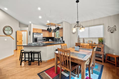 Open-concept dining and kitchen area featuring a rustic wooden dining table, modern light fixture, and a granite breakfast bar with barstool seating—perfect for family meals and entertaining.