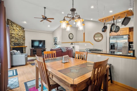 Rustic dining space featuring a wooden table for six, stylish overhead lighting, and an open view into the kitchen and living area. Ideal for family meals and entertaining.