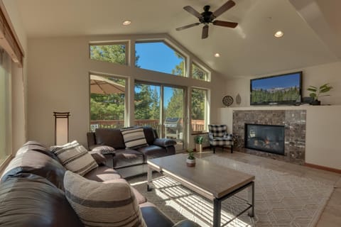 - Living room with vaulted ceilings and fireplace warmth  
- Large windows with forest views and natural light  
- Cozy leather sofas and flat screen TV setup