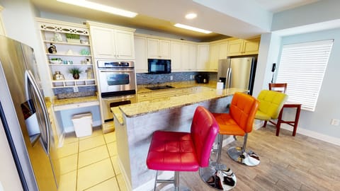 Kitchen featuring granite countertops, modern appliances, and colorful bar seating.