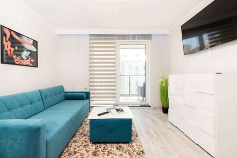 A modern living room with a turquoise sectional sofa, a large wall-mounted flat-screen TV, and minimalistic white decor. 