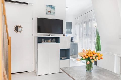A bright and airy dining or living room featuring a small coffe table with flowers as a centerpiece. There is a flat-screen TV on the cabinet. 