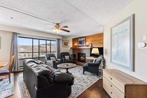 Relax in your cozy living room with a crackling fireplace and stunning mountain views through floor-to-ceiling windows.