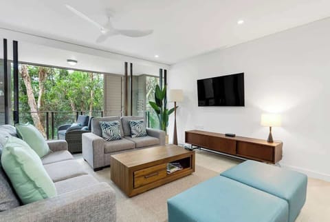 Stretch out in the inviting living area where contemporary comfort meets lush green surrounds, with natural light streaming through expansive sliding doors.