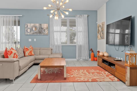 Unwind in your stylish living space with modern furnishings, vibrant coral accents, and a striking sunburst chandelier overhead.