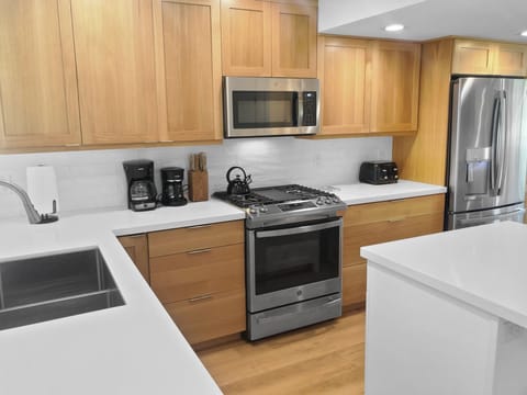 Prepare meals in our fully equipped kitchen, featuring stainless steel appliances, white countertops, and wood cabinetry. All the essentials for a great stay.