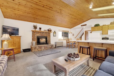 Cozy mountain living room with wood ceilings, stone fireplace, comfy seating, and smart TV—perfect for relaxing evenings, movie nights, and warm cabin vibes after outdoor adventures.