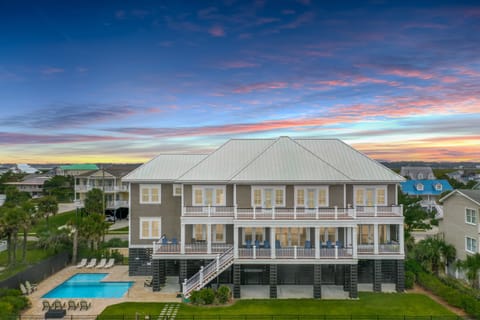 Stunning beachside property featuring multiple balconies, private pool, and coastal architecture under vibrant sunset skies.
