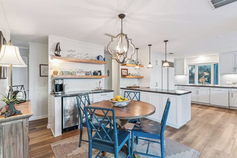 Your spacious gourmet kitchen invites culinary adventures with white cabinets, dark countertops, and charming blue dining chairs around a warm wooden table.