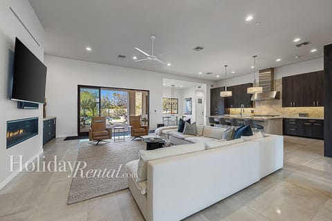 Open living area with comfy seating, large TV, and a sleek kitchen island