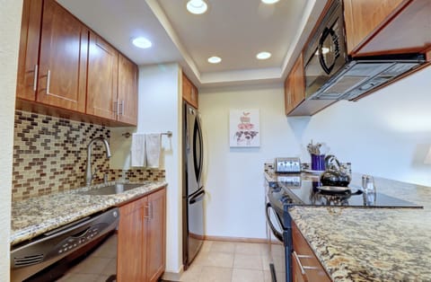 A small kitchen with granite countertops, wooden cabinets, stainless steel appliances including a refrigerator, dishwasher, oven, and microwave, and a mosaic tile backsplash.