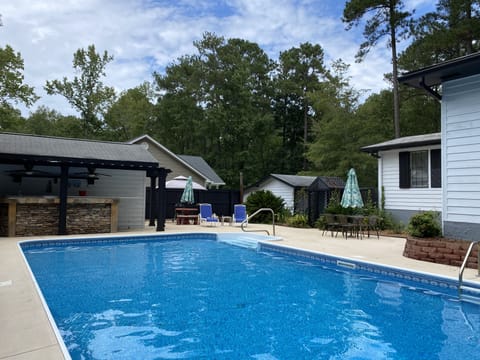 Pool with lounge chairs, table with umbrella and charcoal grill.