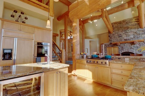 Spacious kitchen with wooden cabinets, granite countertops, and stainless steel appliances, including a refrigerator and stove. Stone accent wall with built-in oven and log beams overhead.