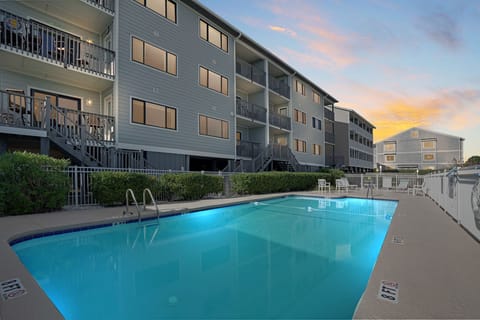 Multi-story beachside building with balconies surrounding a crystal-clear swimming pool during golden hour.