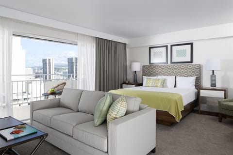 Step into your bright, modern suite where the bed beckons with crisp linens and the sofa invites you to unwind with a view of the city skyline stretching beyond your private balcony.