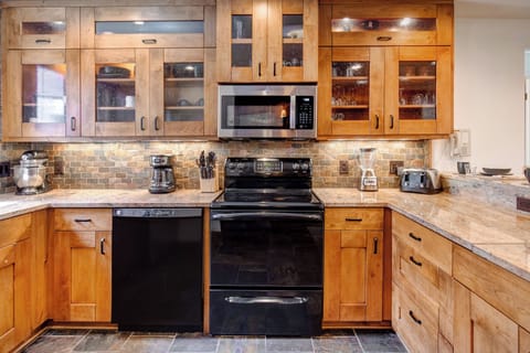 Warm wood cabinets, undermounted lighting, black and stainless appliances, and in cabinet lighting in glass doors.