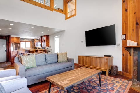 Blue upholstered couch with green and white throw pillows, warm wood toned coffee table and TV hutch and flat screen TV.