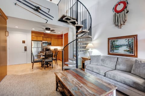 Snow Flower 31's living room with grey upholstered couch, spiral staircase and mixed color wood coffee table.