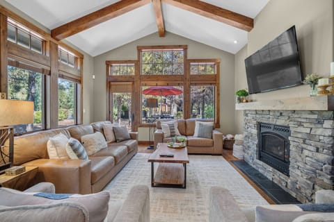 Gather in your sun-filled living room with soaring ceilings, exposed wood beams, and a stunning stone fireplace. Large windows frame views of the surrounding trees, while plush seating invites you to relax and unwind in comfort.