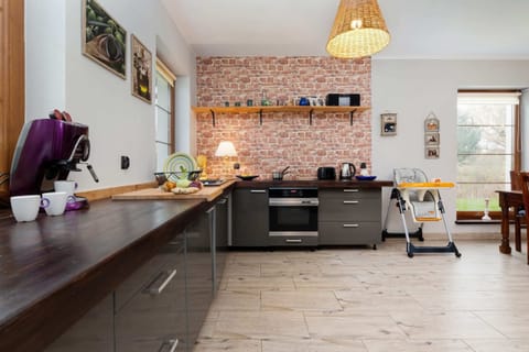 A modern kitchen with black cabinets, a wooden countertop, and a rustic brick backsplash, adjacent to the dining area.