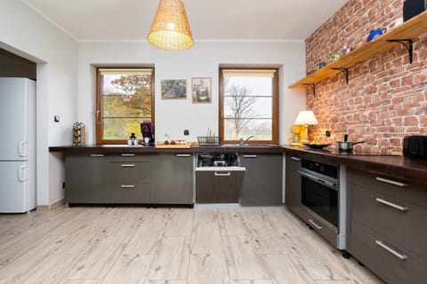 A modern kitchen with dark gray cabinets, a wooden countertop, and a rustic brick backsplash, adjacent to the dining area.