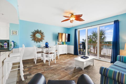 Relax in your bright coastal living space with ocean-themed decor, tropical ceiling fan, and private balcony overlooking swaying palms.