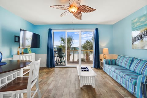 Relax in your bright coastal living room with stunning balcony views of swaying palms and blue skies.