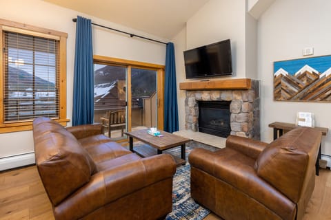 Cozy up by your stone fireplace with mountain views through the window, perfect for après-ski relaxation.