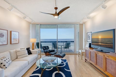 Glass doors open to a balcony with ocean views, framed by hardwood floors and a white sofa.