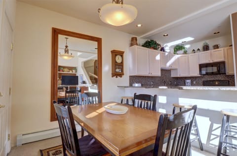 A kitchen and dining area with a wooden table and chairs, a countertop with barstools. Bright lighting from ceiling fixtures illuminates the room.