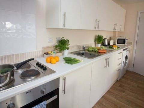 Long white kitchen with modern cabinetry, oven, fresh herbs, and orange fruit in serviced apartment – Castle 6 - Southampton