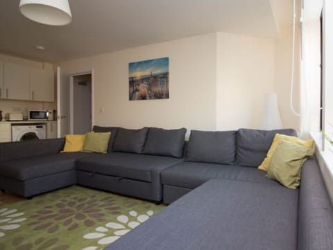 Spacious living area with large sectional grey sofa, yellow cushions, wall art, and green accent rug – Castle 6 - Southampton