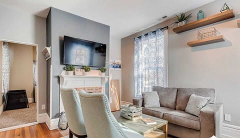 - Stylish living room with a mounted TV over the fireplace and bright natural light
- Plush sofa and two accent chairs make this space perfect for gathering and lounging
- Floating shelves and unique details bring warmth and charm