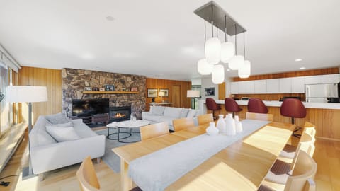 Relax in your open-concept living space featuring a cozy stone fireplace, modern entertainment center, and stylish dining area bathed in natural light—perfect for memorable gatherings.