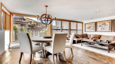 Picture yourself sharing meals at this elegant round dining table, natural light streaming through floor-to-ceiling windows framing mountain views, then relaxing in the adjacent living area with cozy throws and a warm, inviting atmosphere.
