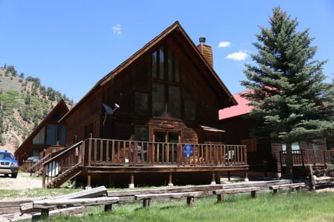 A charming A-frame cabin with inviting wooden deck, nestled among evergreens and scenic mountain views, marking the welcoming entrance to your mountain retreat.