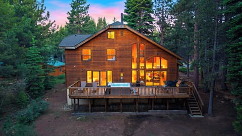 Twilight mountain lodge with a spacious deck, private hot tub, and warm forest-side glow.