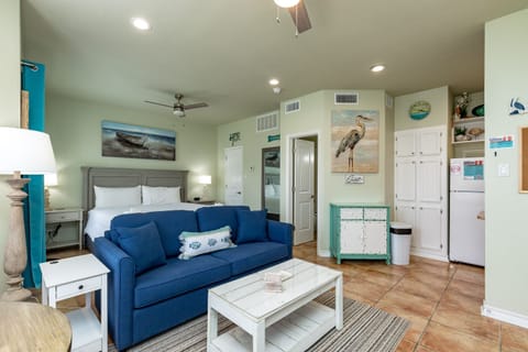 Relax in your coastal-themed studio with ocean artwork, plush blue sofa, and convenient kitchenette for your beach getaway.