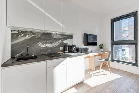 A contemporary kitchen with a black marble backsplash, white cabinetry, and essential appliances. Large windows ensure a bright cooking environment.