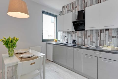 A compact kitchen with sleek gray cabinets and a decorative backsplash. A vase with flowers adds a welcoming touch to the minimalist design.