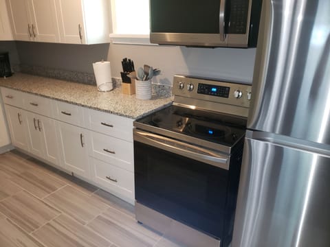 Kitchen refrigerator and stove/oven. Glass top stove with pots/pans provided.
