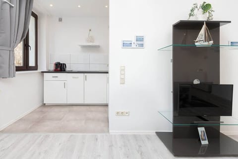 View from the living area with black bookcase to the kitchenette with white furniture.